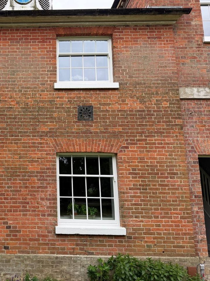 A red-brick wall with a tall sash under a curved brick arch on the ground floor and a shorter sash on the floor above