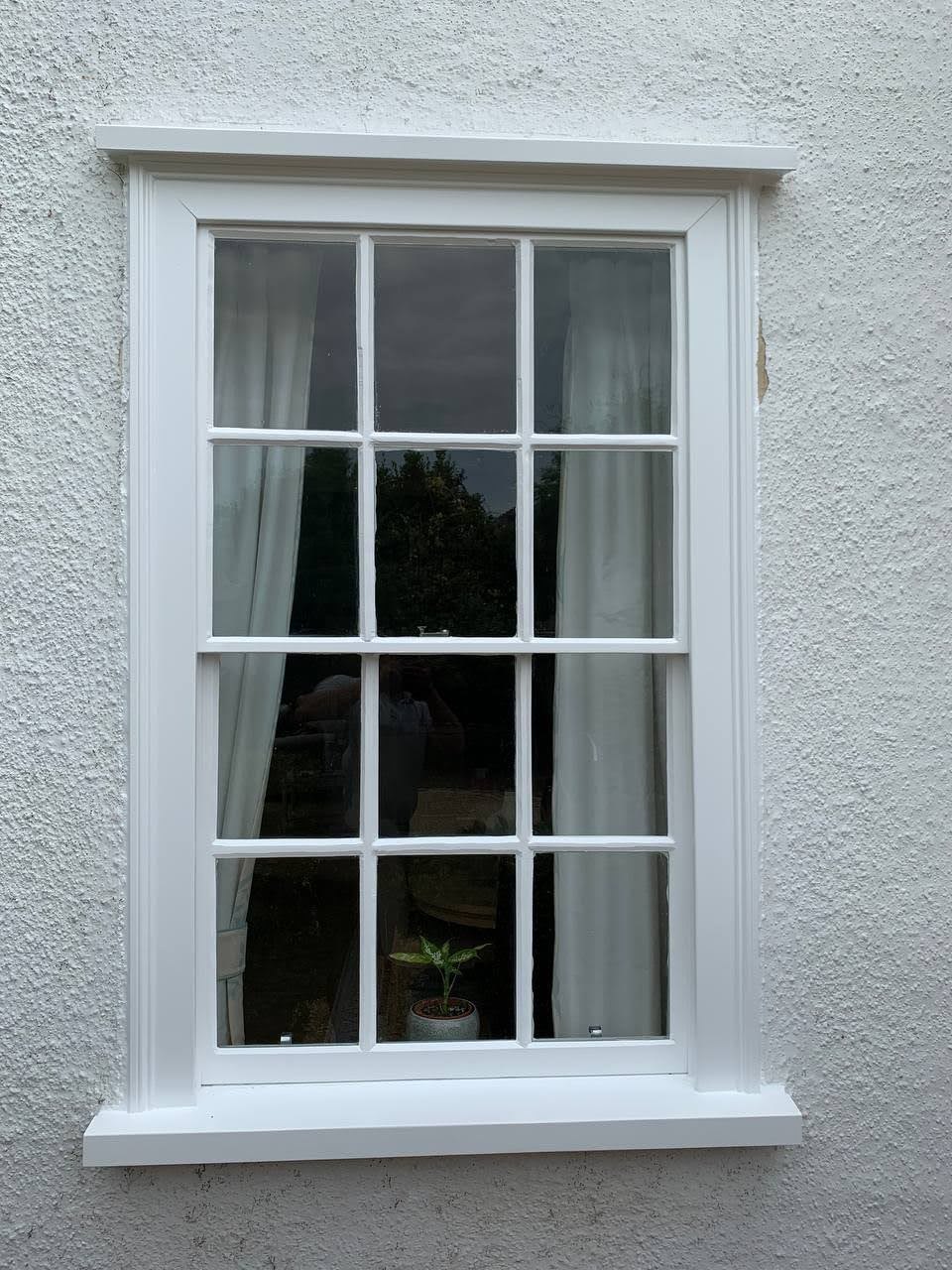 A white six-over-six sash window in a rendered wall, freshly painted