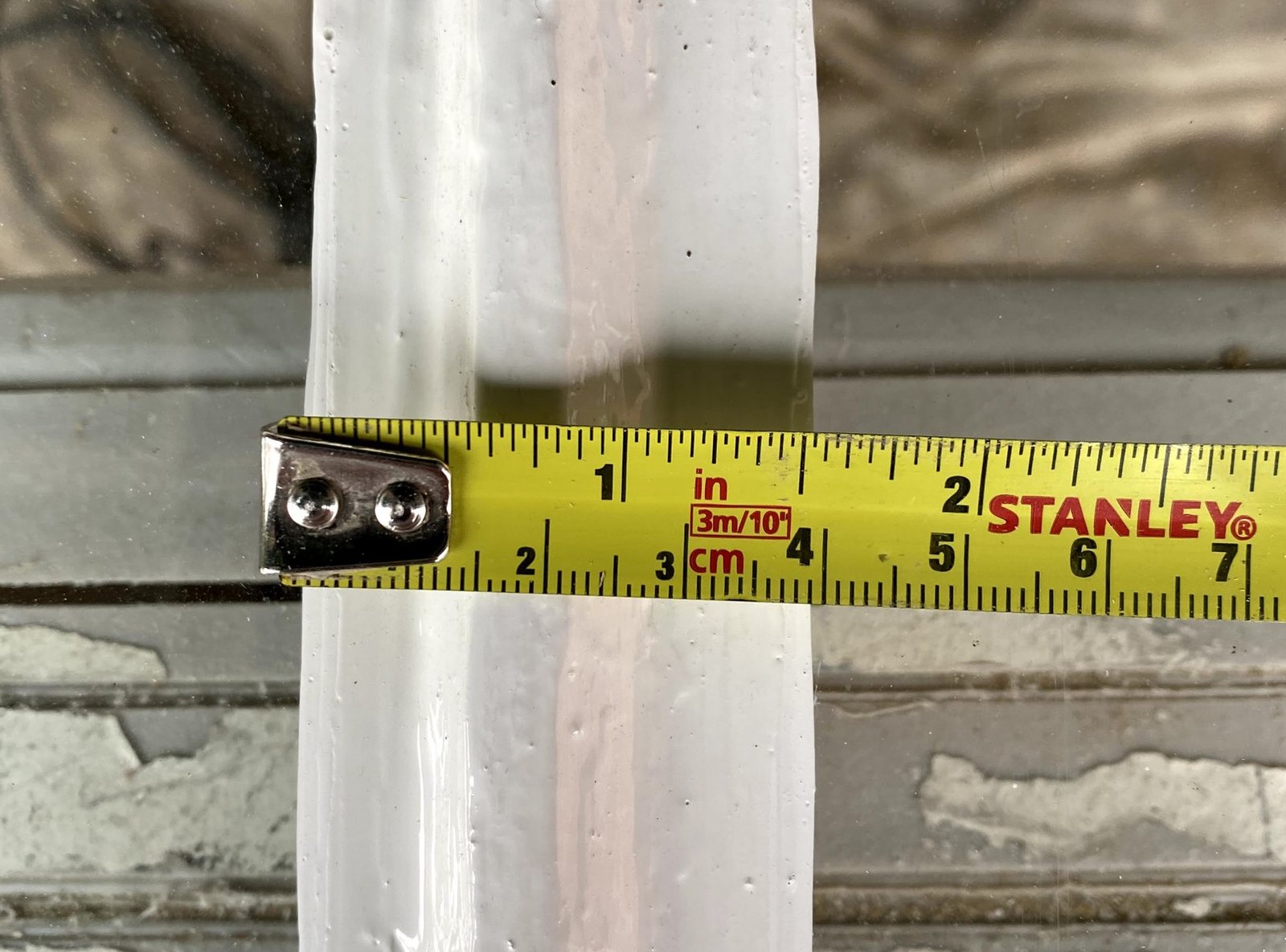 A tape measure held across a painted glazing bar of a sash window, the old glass and putty either side