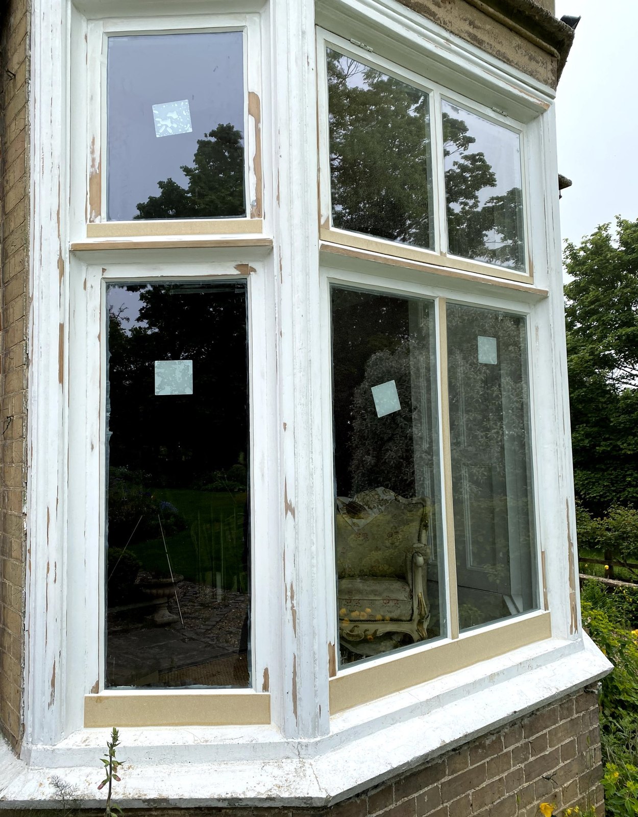 A bay of one-over-one sash windows during restoration, old white paint on the frames and new pale timber along the sash rails