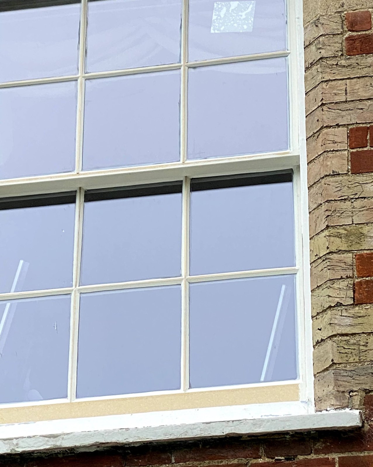 A six-over-six sash window in a red-brick and gault-brick wall, with new glass and a pale strip of Tricoya laminated along the bottom rail before painting