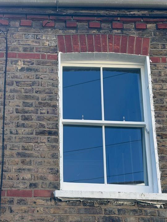 A white two-over-two sash window under a red brick arch in a yellow stock-brick wall