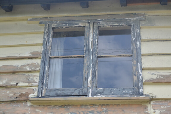 Two-light timber cottage casement window with badly flaking paint, set in peeling cream weatherboarding