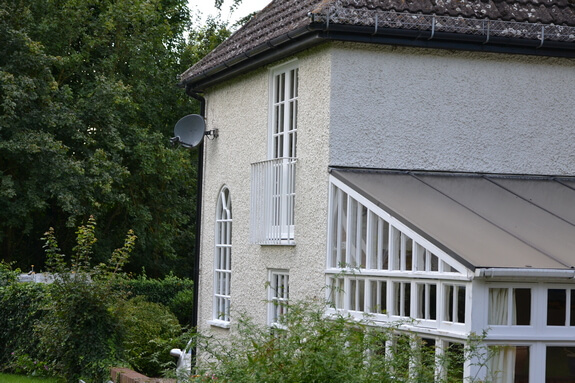 Rendered house with white-painted timber windows, including a tall arched window, and a white conservatory