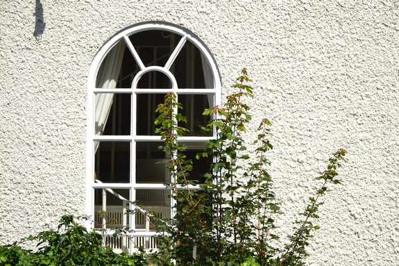 Arched timber window painted white with radiating glazing bars in a textured rendered wall, after restoration