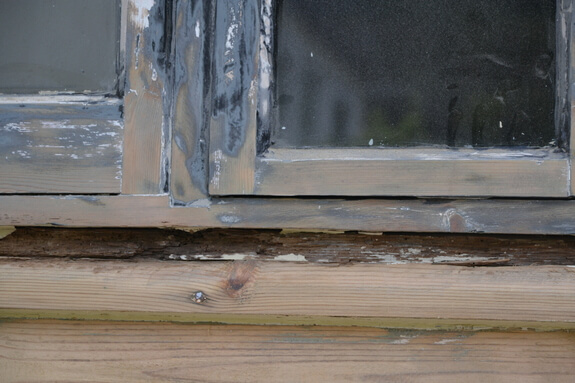 Close-up of flaking paint on the bottom rail of a cottage casement window above weathered timber cladding