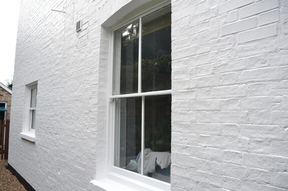 Two-over-two white sash window in a white-painted brick wall