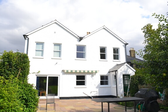 Rear of a house with white-painted brick walls, sash windows, sliding patio doors and a striped awning