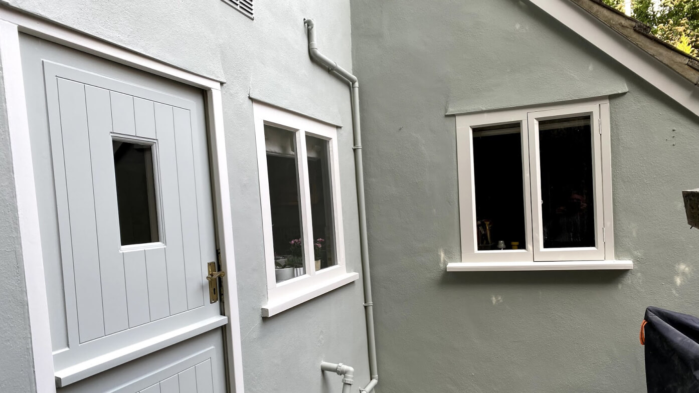 Pale grey boarded stable door with a small glazed panel beside white timber casement windows on grey walls