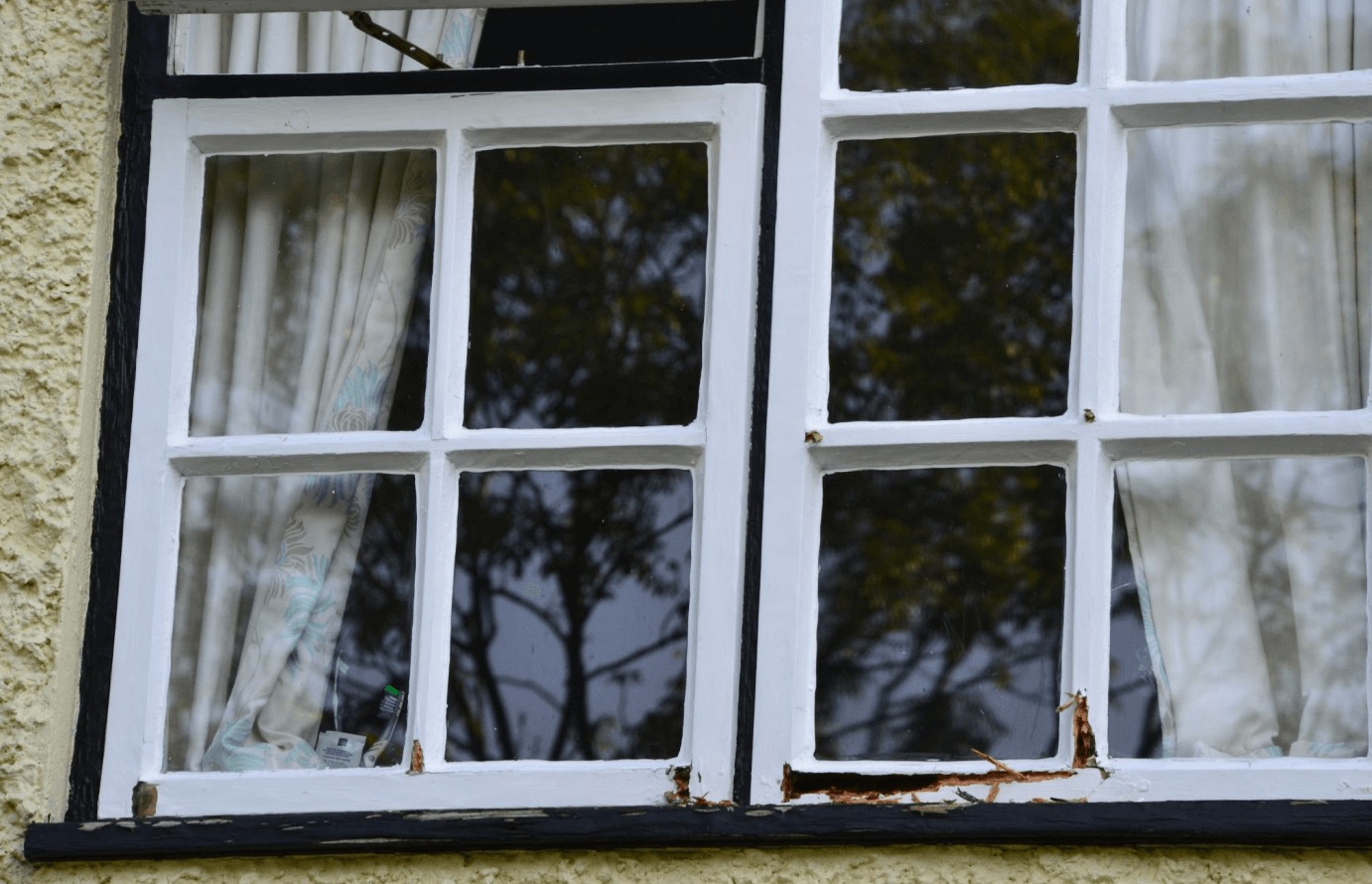 A painted sash window with rot breaking through at the bottom rail