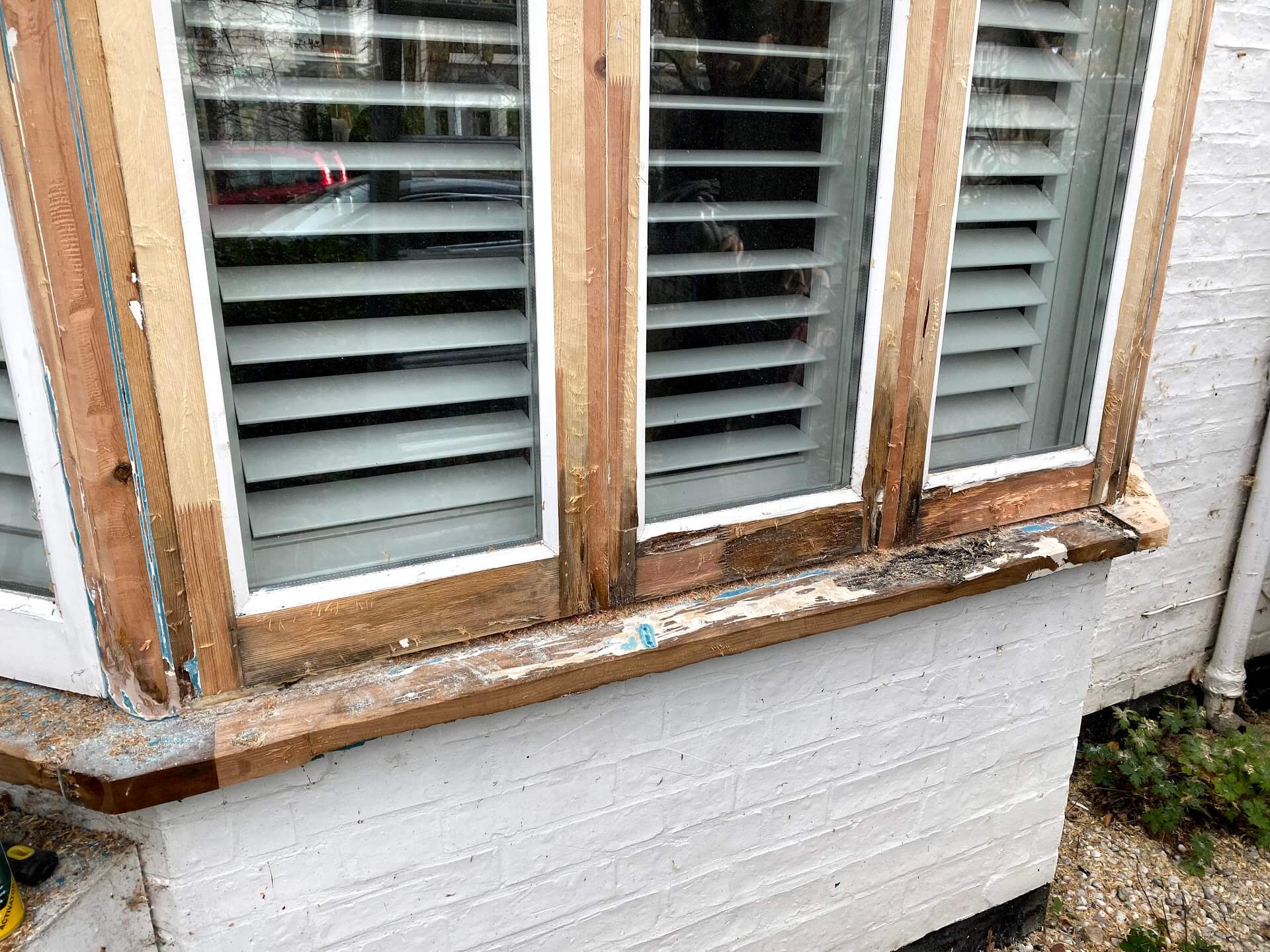 Casement window frames stripped to bare timber, with a sill still patched with old paint and filler