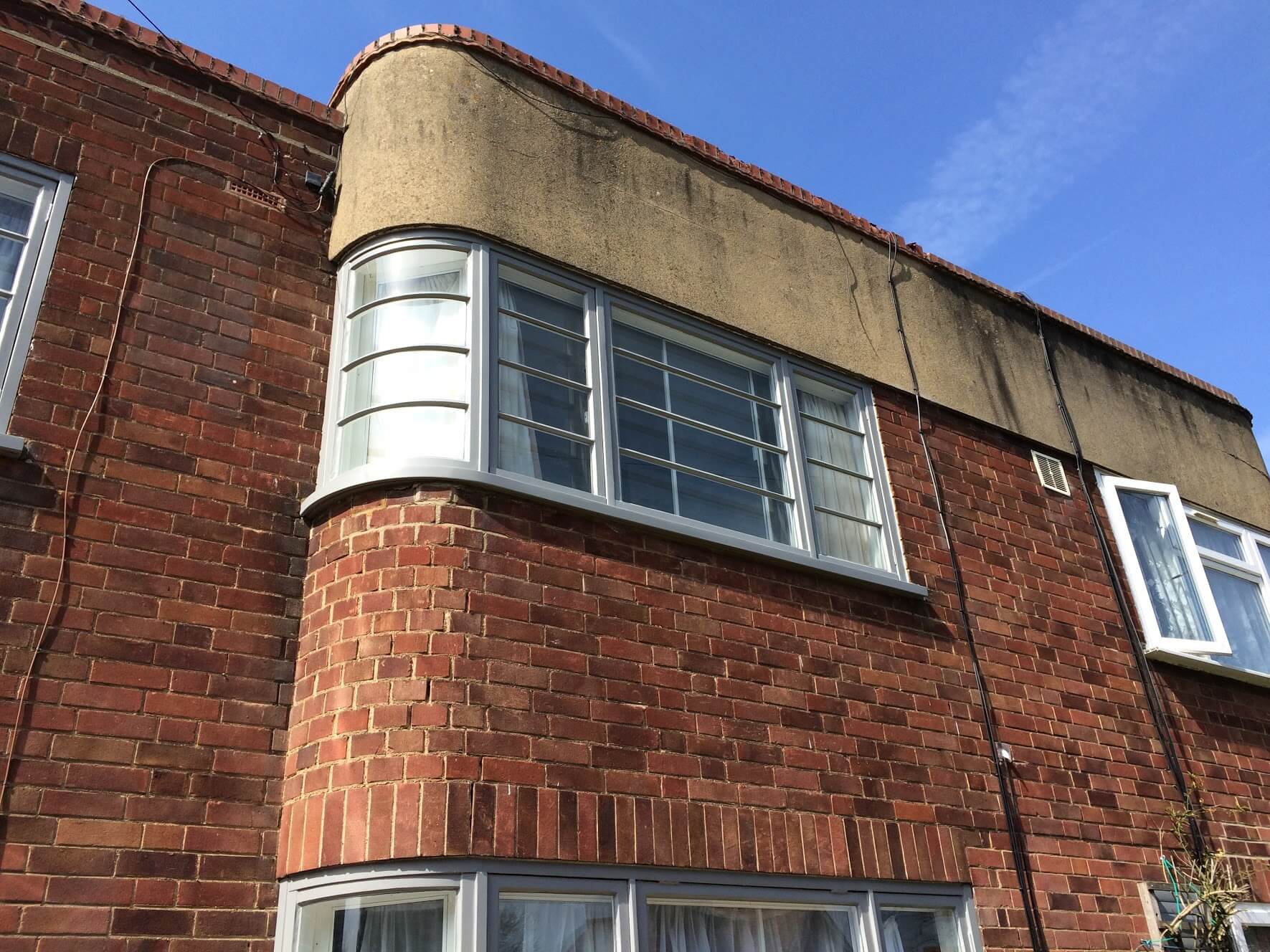 Curved red brick Art Deco bay with pale grey timber windows, horizontal glazing bars and curved corner glass