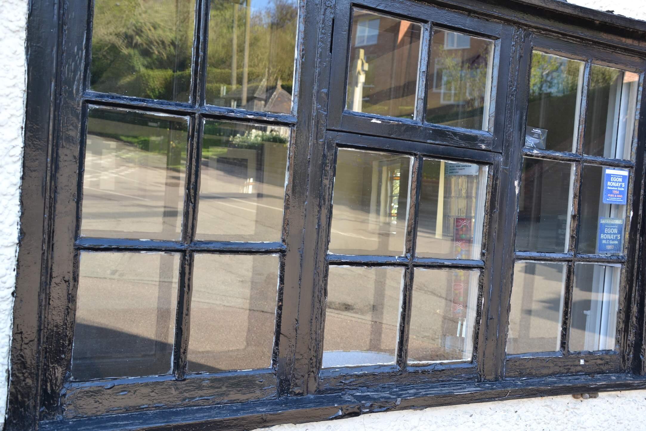 Small-paned timber casement window with weathered black paint and a decayed sill, in a white-rendered wall