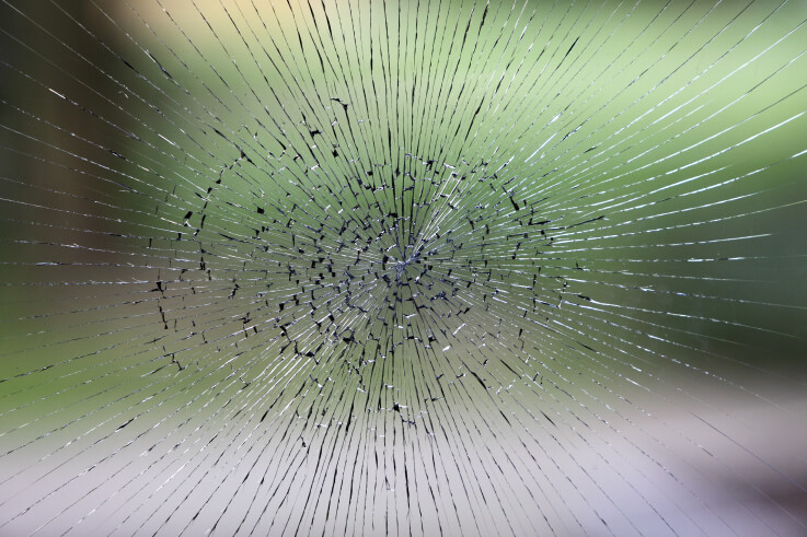 A pane of glass shattered from a central point, cracks spreading outwards