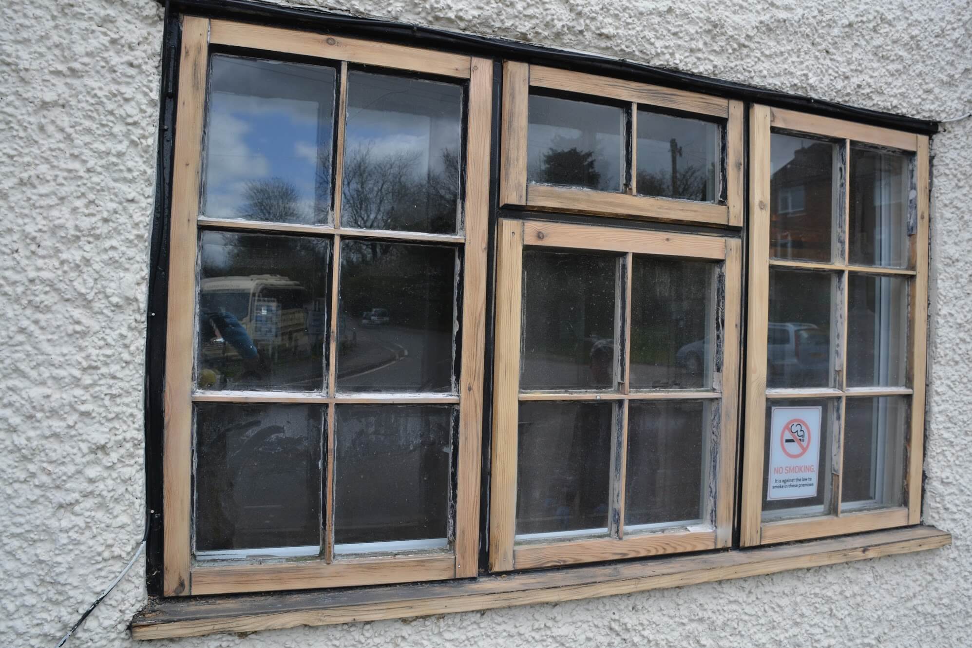 Small-paned timber casement window sanded down to bare wood in a white textured render wall, ready for painting
