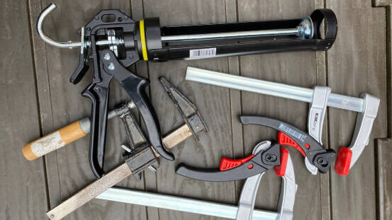 Two long clamps and a sealant gun on decking