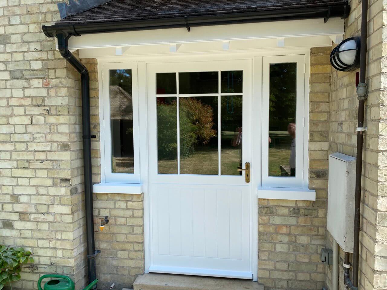 Half-glazed timber door and side lights repainted white beneath a small porch canopy in a buff brick wall