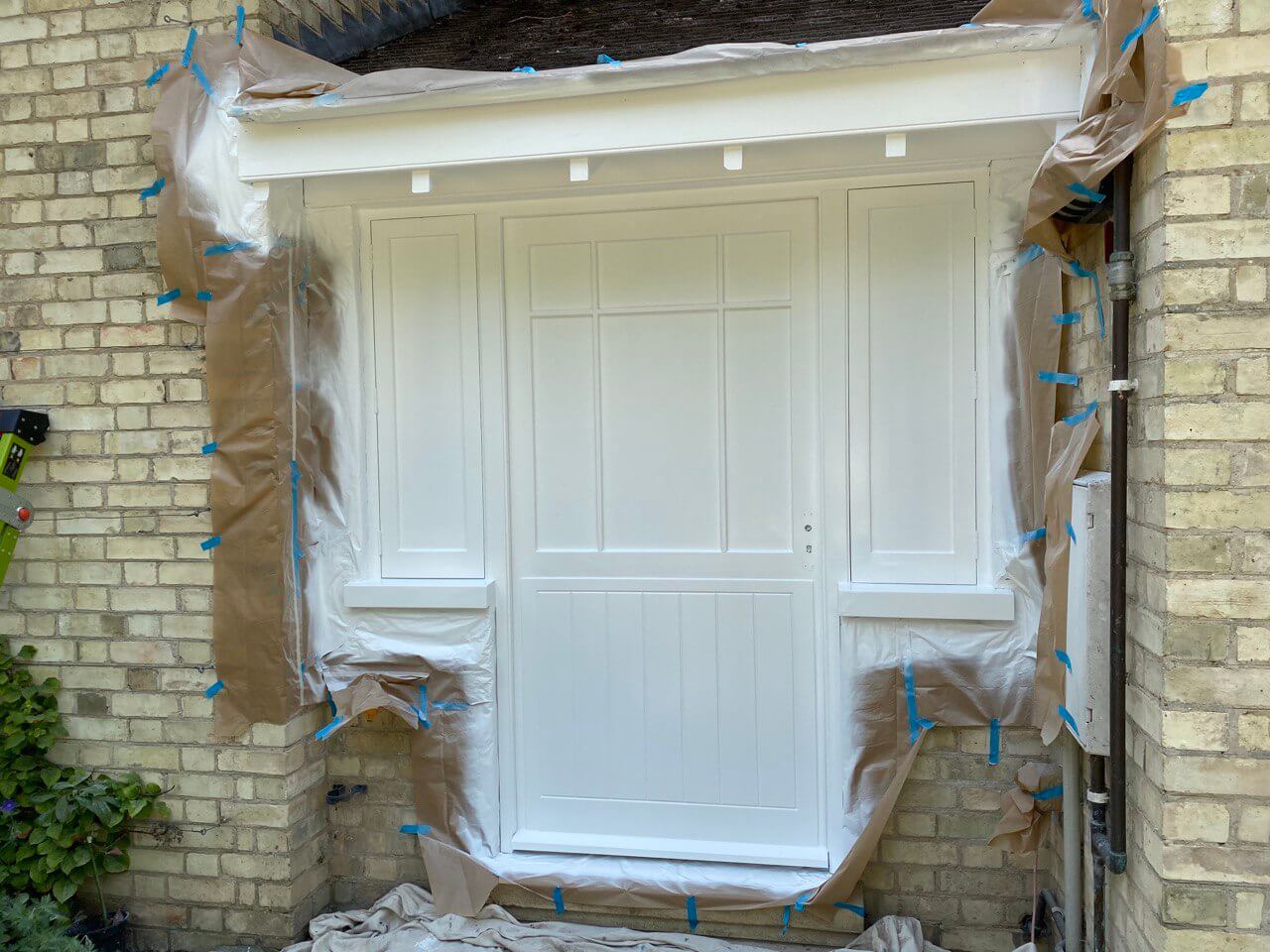 Half-glazed door and side lights spray-painted white, the surrounding brickwork masked with paper, plastic and tape