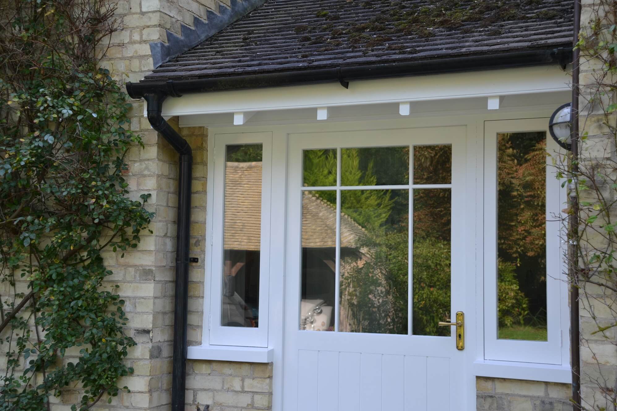 White-painted timber porch with a half-glazed front door and side windows under a tiled roof