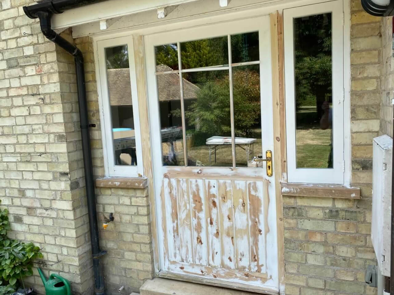 Half-glazed timber back door and side lights, the lower boarded panel sanded back through worn white paint