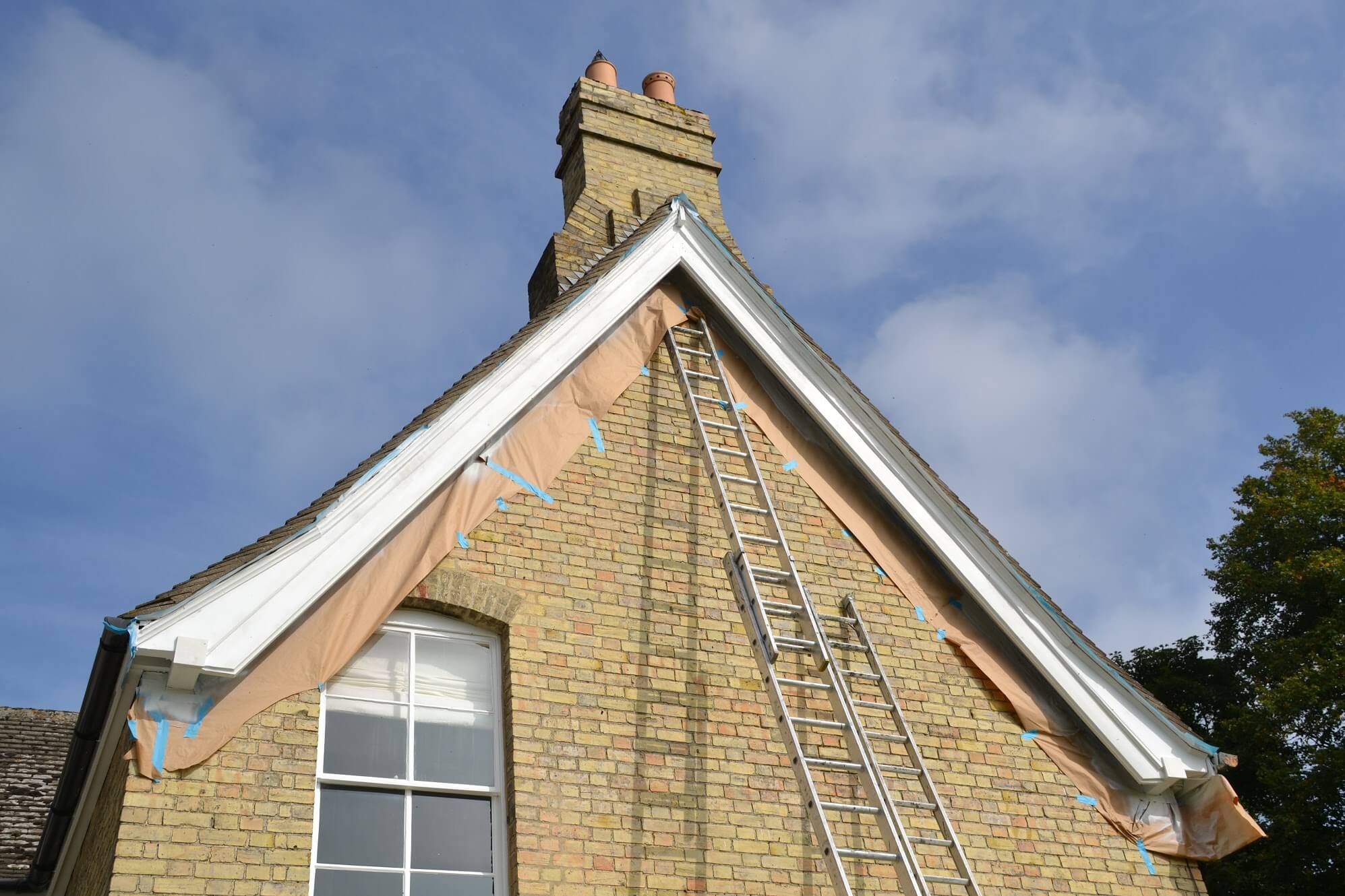 Brick gable with newly painted white bargeboards, masking paper beneath and a ladder against the wall