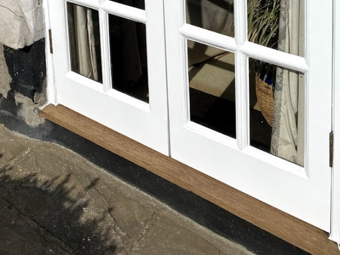 A weathered hardwood sill under white glazed patio doors