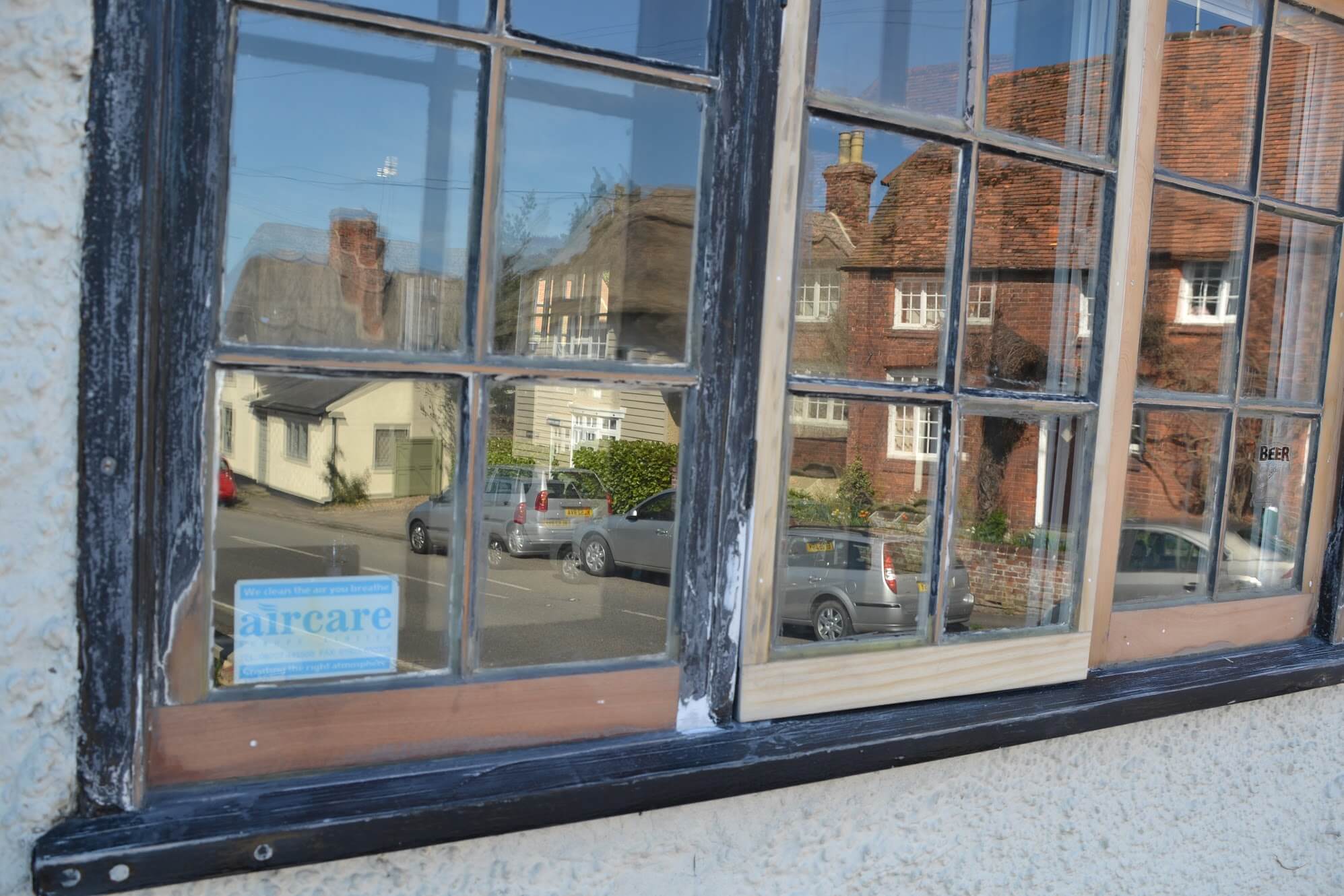 Close-up of a pub casement window: flaking black-painted frame beside an opening casement in bare timber