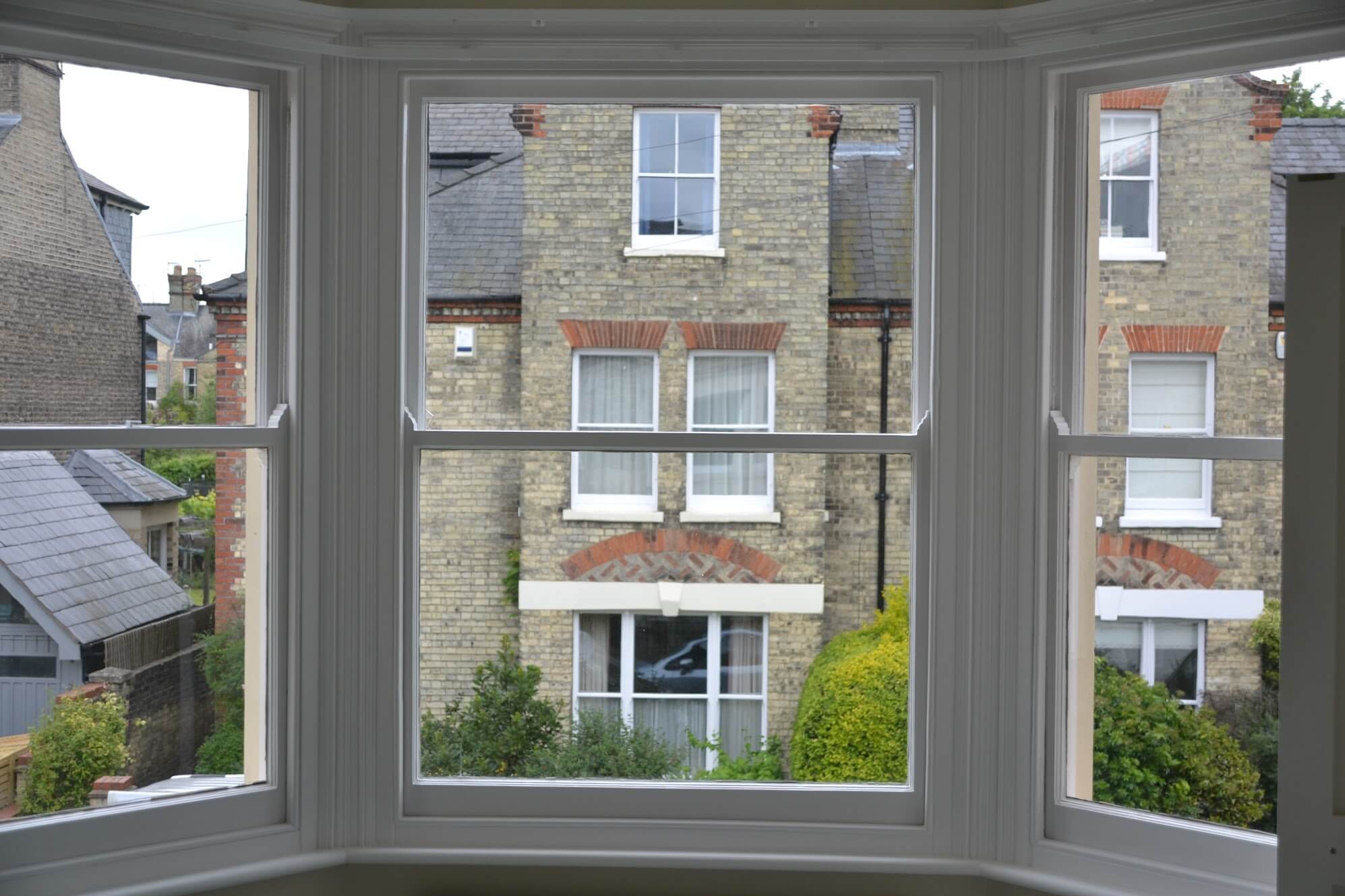 A bay of three sash windows seen from inside, with houses across the street