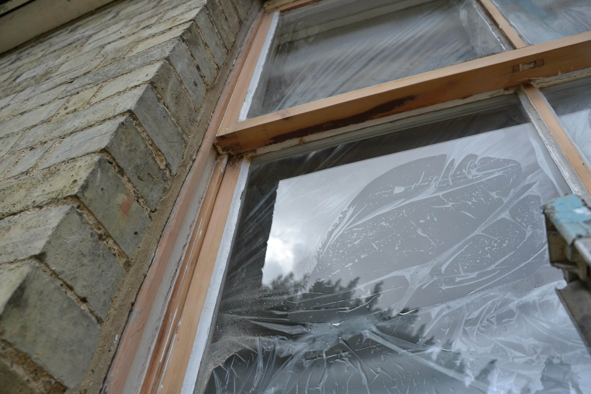 Sash window sanded back to bare timber, its glass covered in protective film, in a buff brick reveal