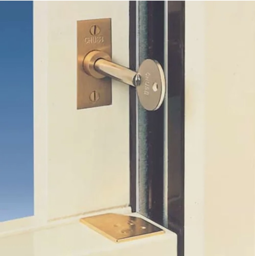 A brass sash stop fitted in a window frame with its bolt pushed in above a white painted sash