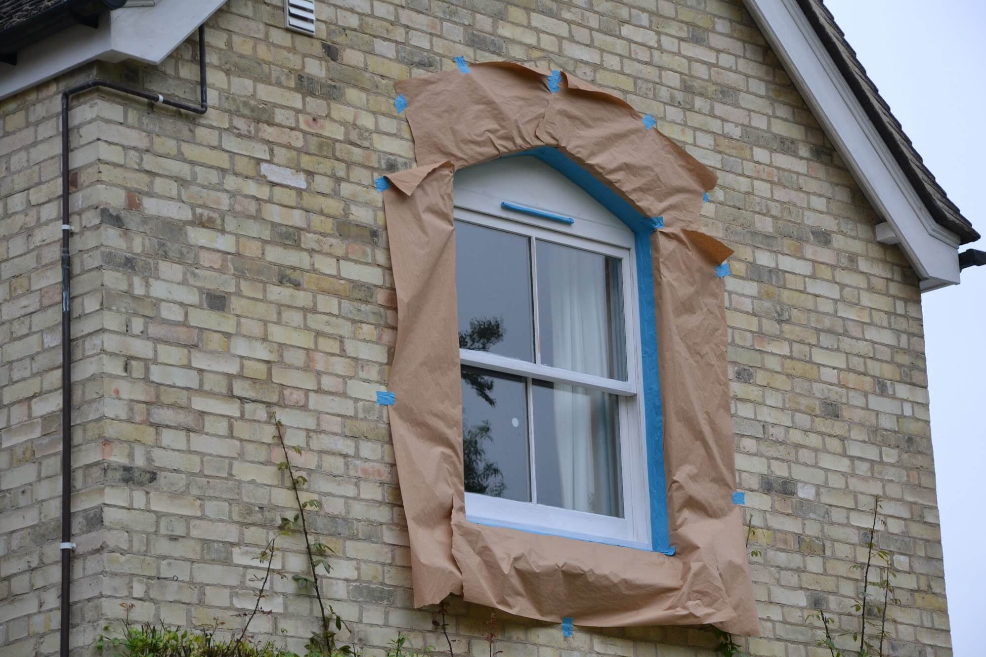 Sash window masked with brown paper and blue tape, its trickle vent taped over before spraying