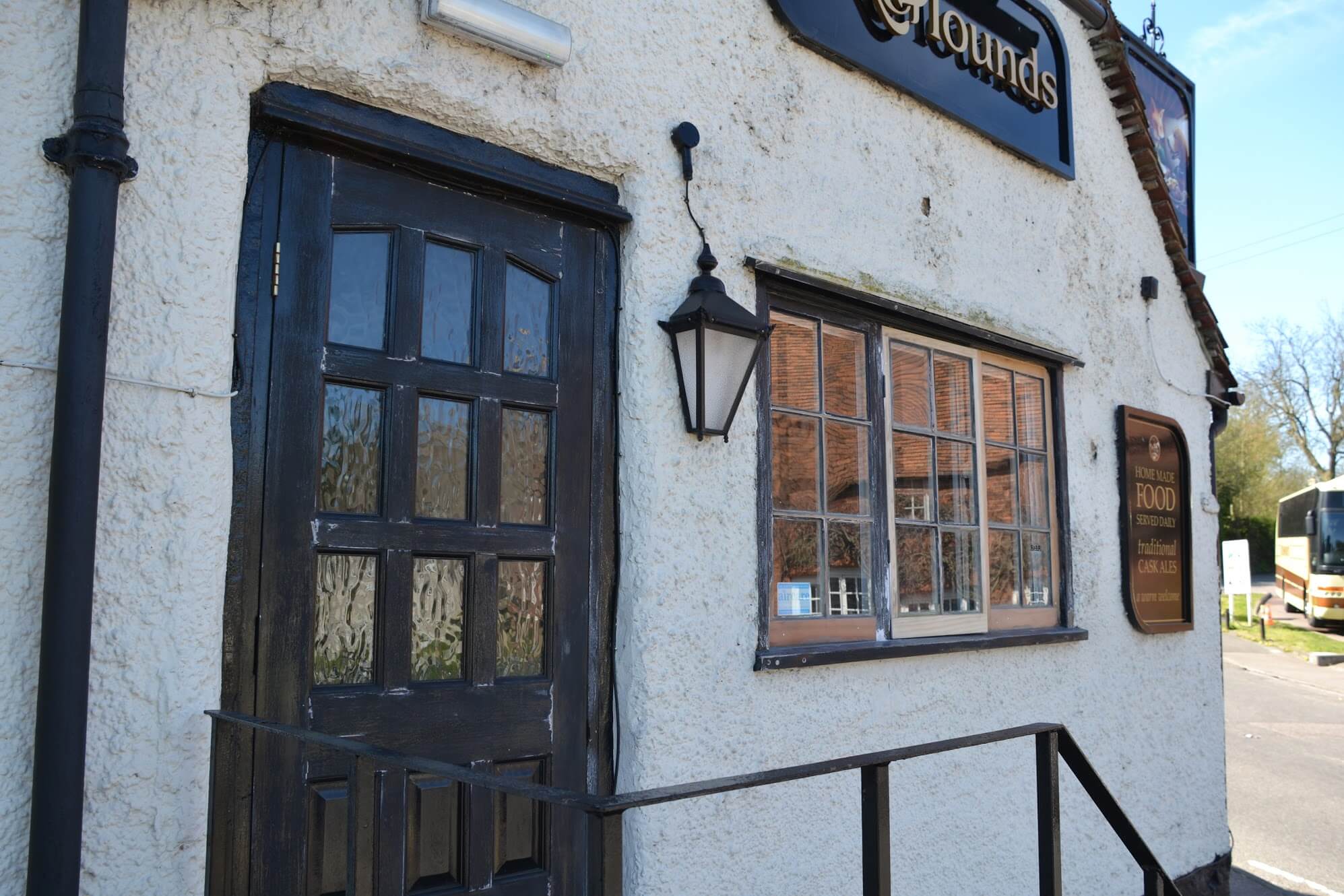 White-rendered pub wall with a dark timber door, black lantern and a small-paned casement window stripped to bare wood