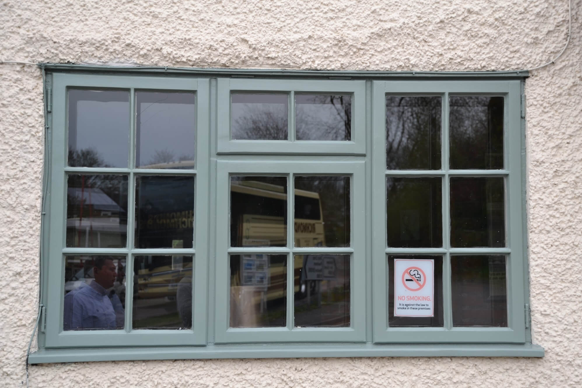 Small-paned timber casement window repainted grey-green in a white textured render wall