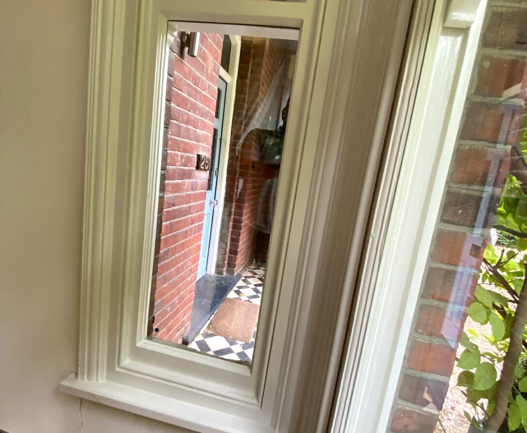 Narrow white-painted timber window with vacuum glazing, seen from inside, facing a brick porch with chequered tiles