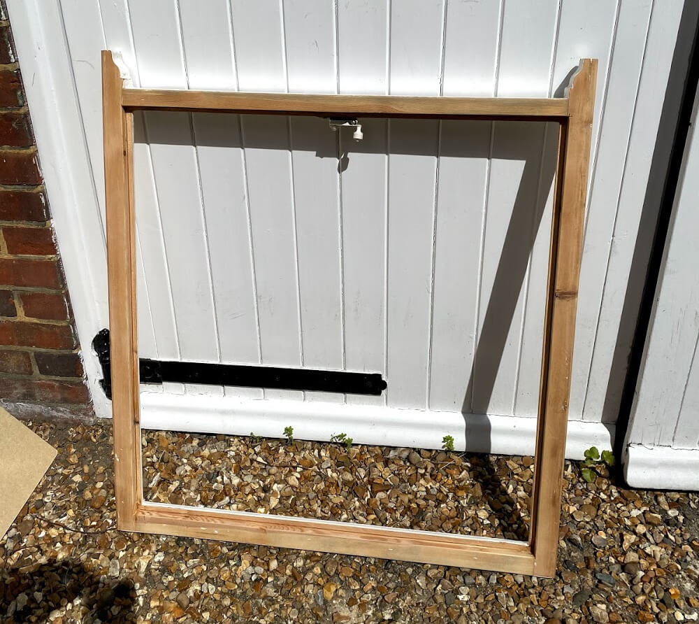 Stripped timber sash with its glass removed and rebates deepened for vacuum glazing, leaning on a white garage door