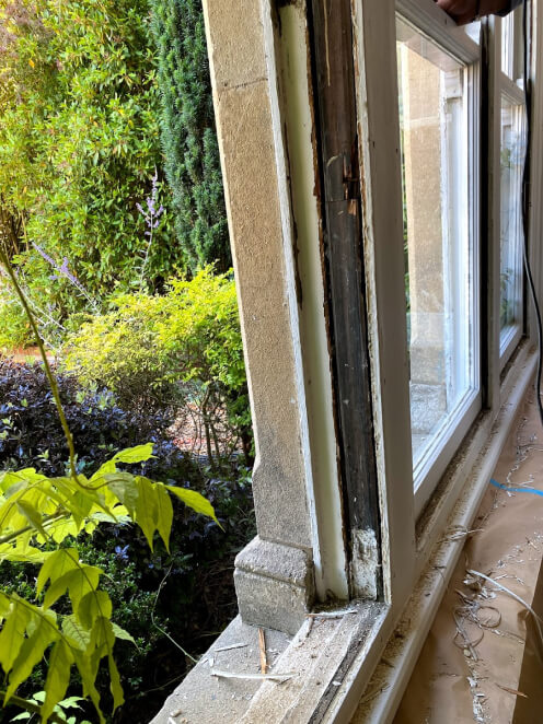 Window opening in a stone surround with the sashes removed, exposing the bare timber box frame, shavings on the sill