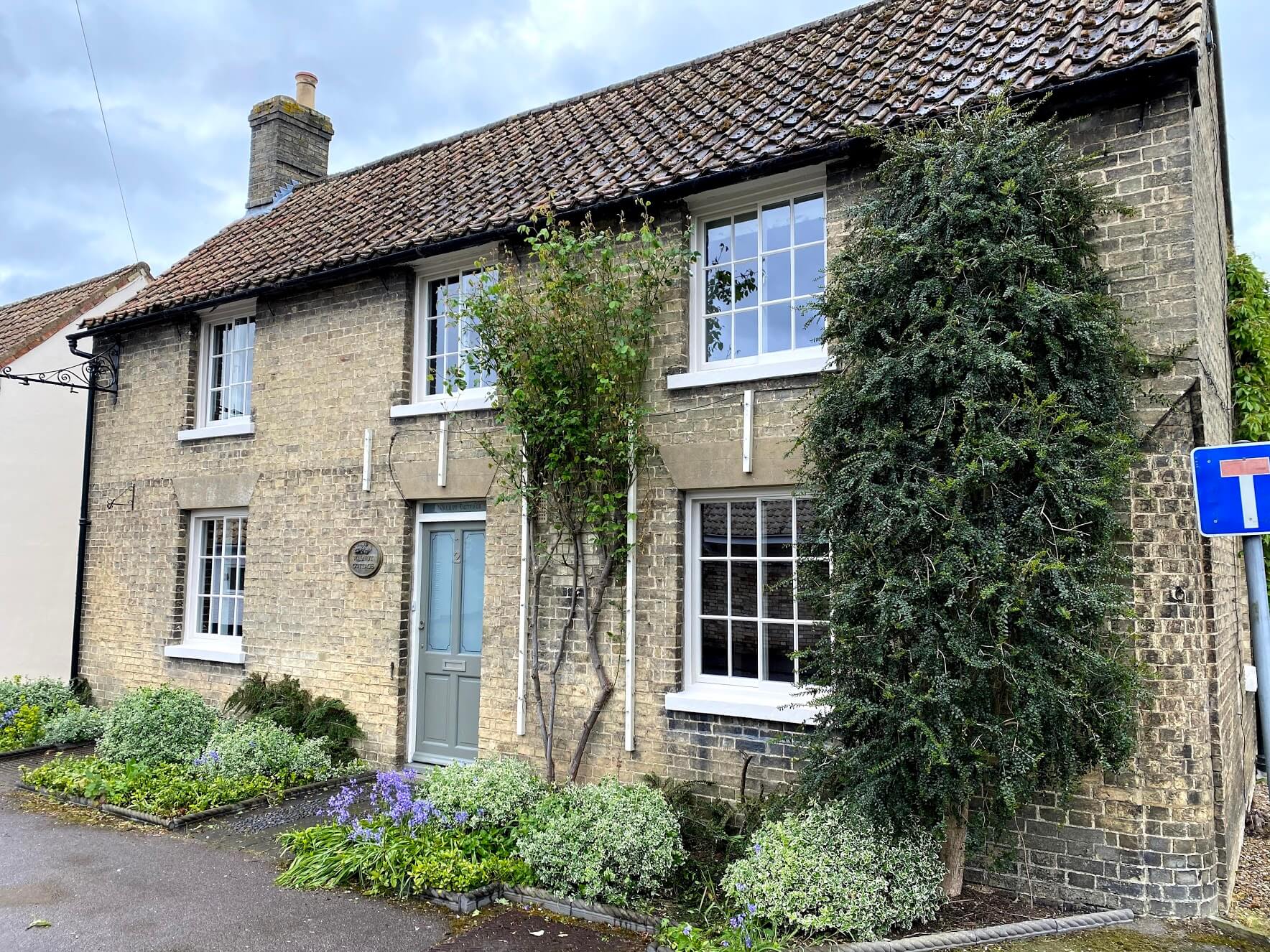 Yellow-brick house with white-painted Georgian sash windows, a grey-blue front door and climbing plants