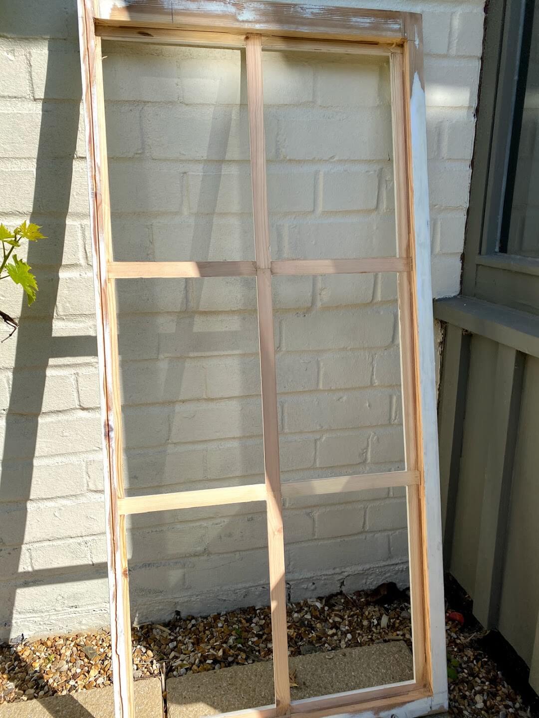 Georgian timber sash with its old single glazing removed, leaning against a white-painted brick wall