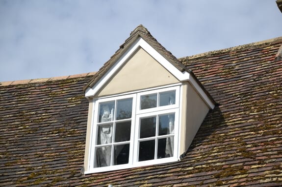 Dormer window with white-painted frames and glazing bars on a mossy tiled roof