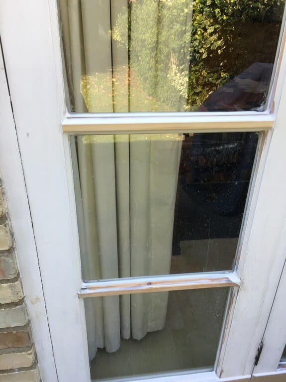Leaf of a glazed timber patio door with worn white paint and one glazing bar sanded to bare wood