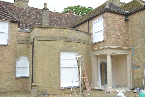 Courtyard elevation during work, windows masked in sheeting and a ladder beside the columned porch