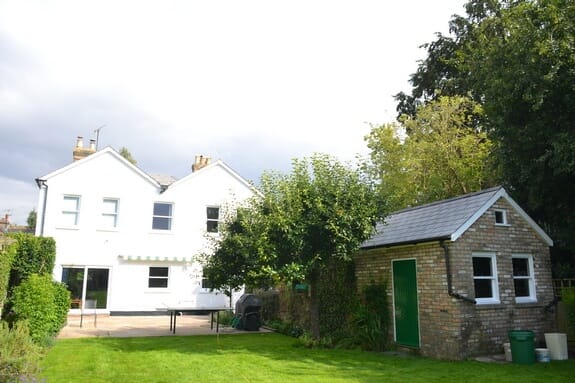 White-painted house and a buff brick outbuilding with a green door and slate roof, seen across the lawn