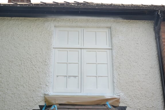 Casement window sprayed white with its glazing masked, in a roughcast wall with paper over the sill