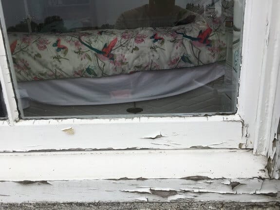 Flaking, cracked white paint on the bottom rail and sill of a timber sash window