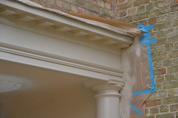 Newly painted porch cornice and column, with masking paper and blue tape protecting the brickwork