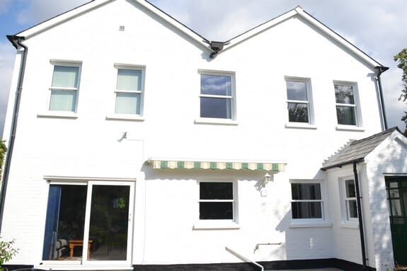 White-painted brick rear wall with two gables, sash windows, sliding patio doors and a striped awning