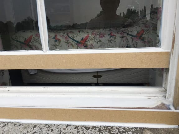 Sash window with its bottom rail and sill front in unpainted timber, the lower sash slightly raised