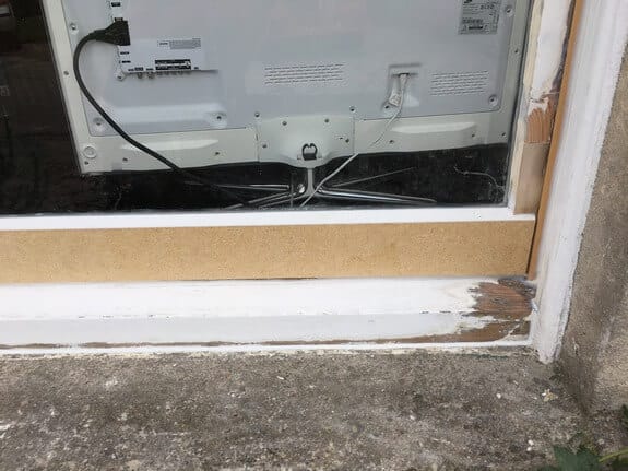 Window bottom rail in unpainted timber above a white-painted sill with a bare, damaged corner