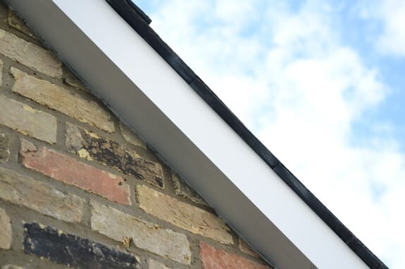 White-painted bargeboard along a roof edge above unpainted buff and red brickwork