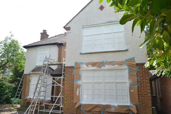 House with rendered upper walls and brick below, windows masked in brown paper, ladders and a scaffold tower